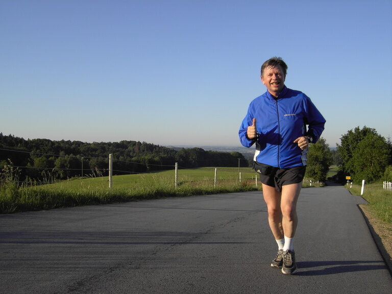 Ein Mann joggt auf der sonnigen Straße und genießt die Natur.