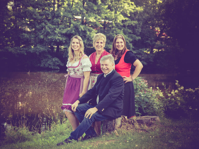 Drei fröhliche Menschen sitzen zusammen auf einer Bank vor einem Bach.